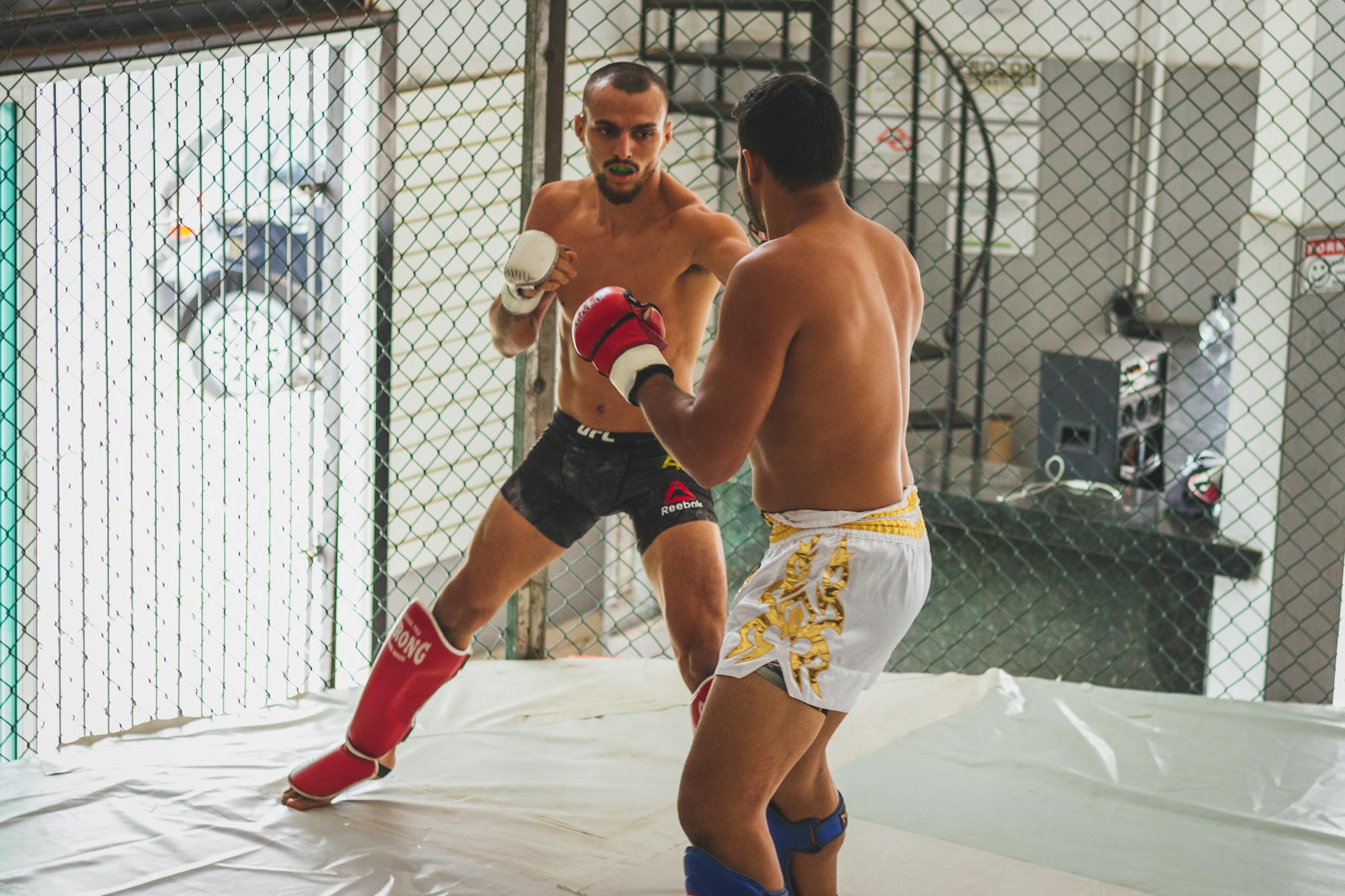 Two men engage in intense kickboxing sparring inside an MMA gym arena.